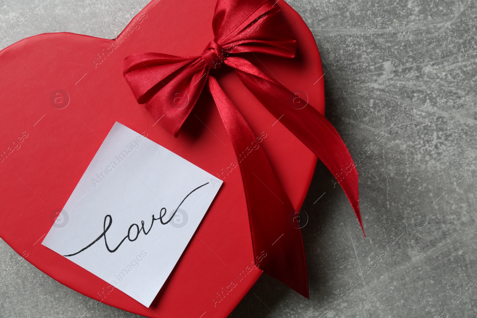 Photo of Heart shaped gift box and sticker with handwritten word LOVE on grey background, top view