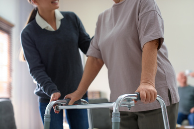 Photo of Care worker helping to elderly woman with walker in geriatric hospice, closeup