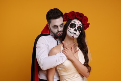 Couple in scary bride and vampire costumes on orange background. Halloween celebration