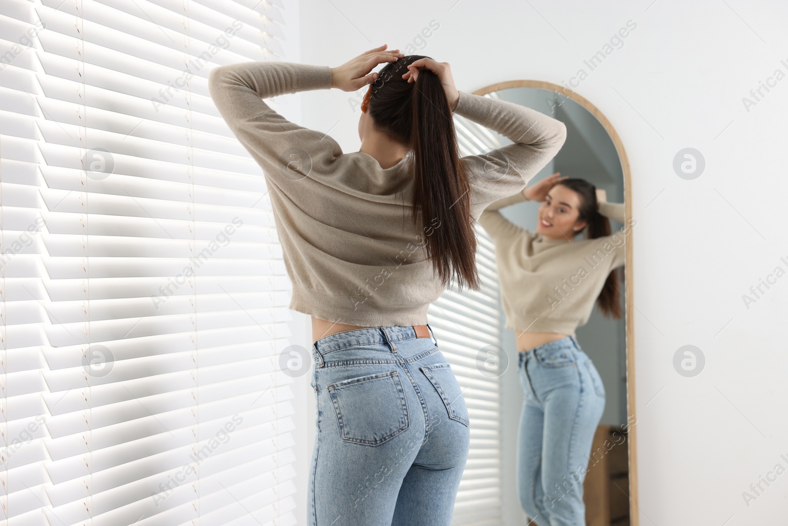 Photo of Young woman in stylish jeans near mirror indoors