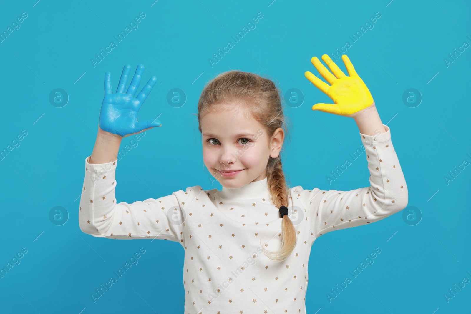 Photo of Little girl with hands painted in Ukrainian flag colors on light blue background. Love Ukraine concept