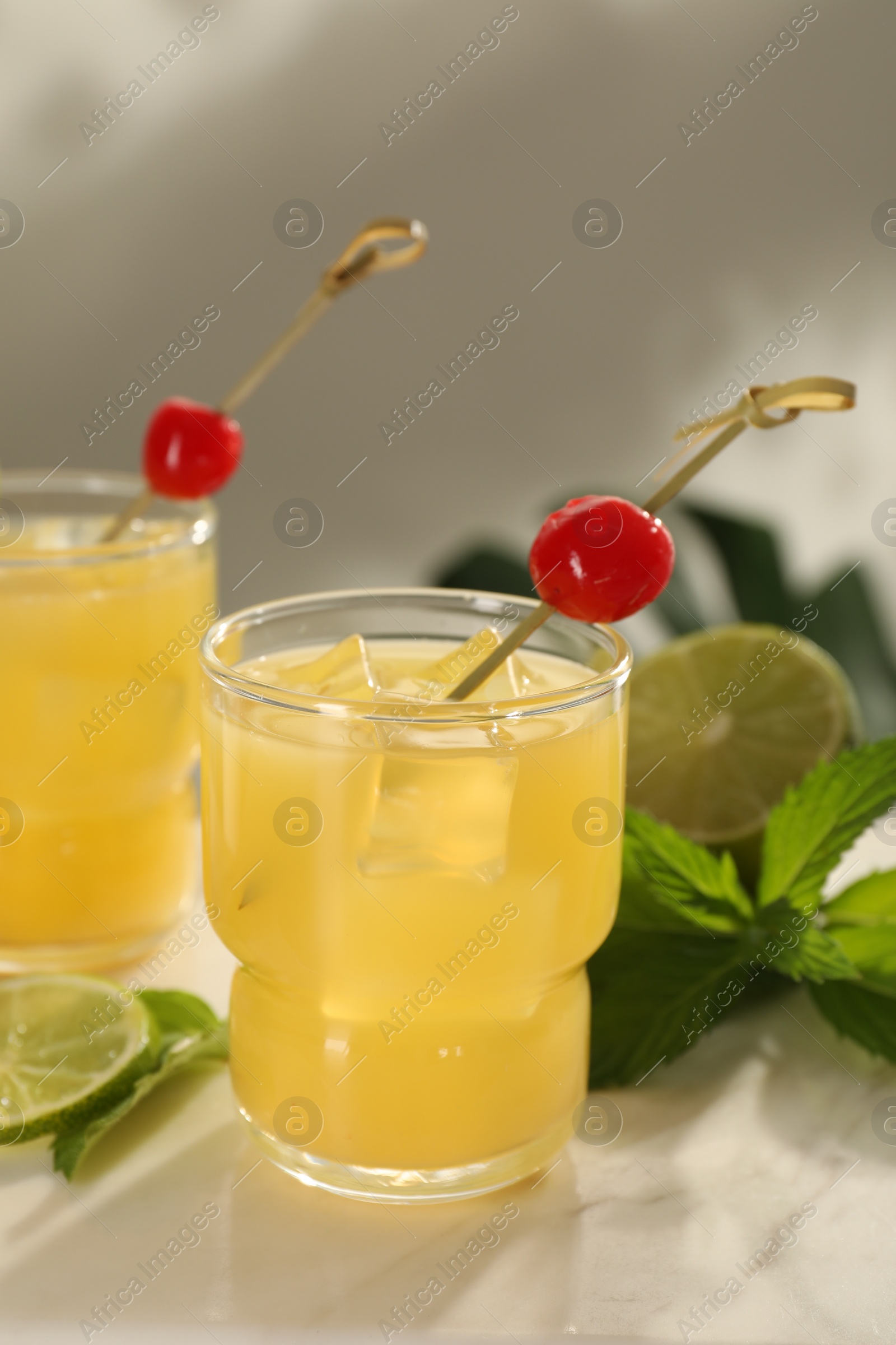 Photo of Glasses of tasty pineapple cocktail with cherry, lime and mint on white table