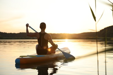 Woman paddle boarding on SUP board in river at sunset, back view