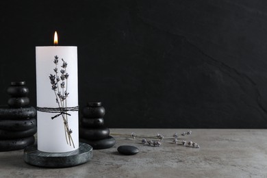 Photo of Burning candle with lavender and spa stones on grey table. Space for text