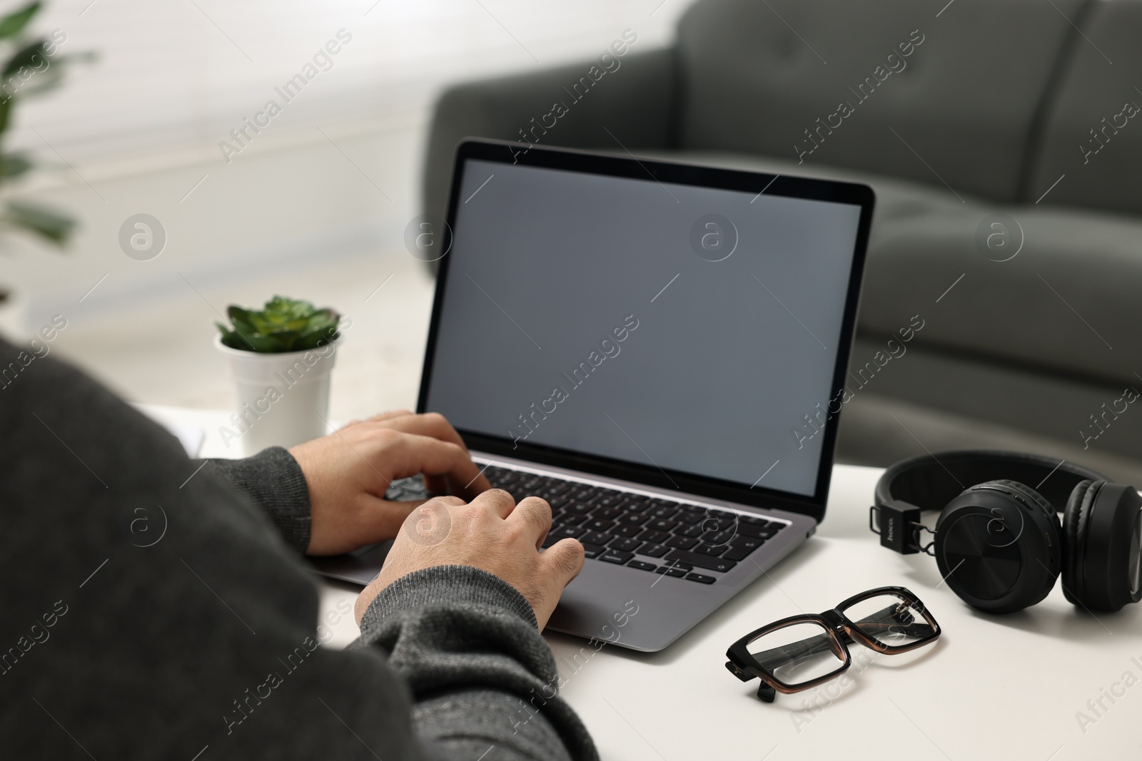 Photo of E-learning. Young man using laptop at white table indoors, closeup