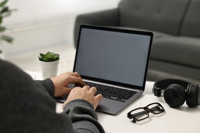 E-learning. Young man using laptop at white table indoors, closeup