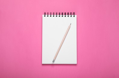 Photo of Blank notebook and pencil on pink background, top view