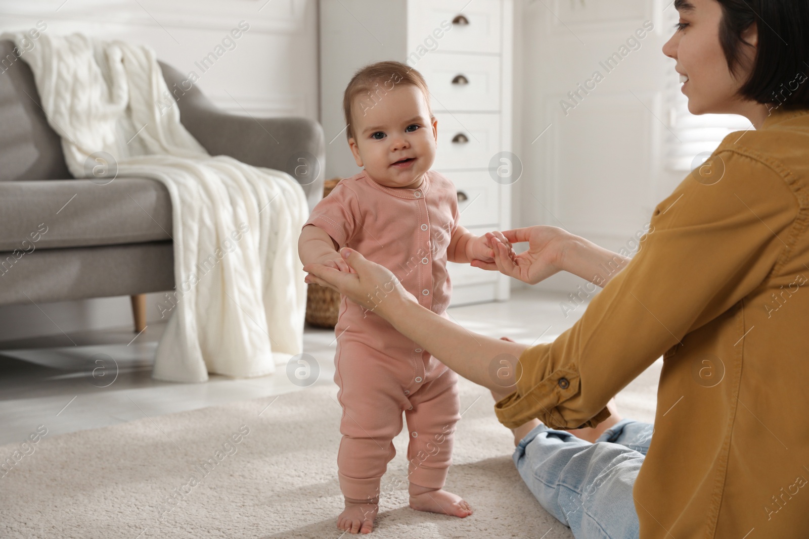 Photo of Mother supporting her baby daughter while she learning to walk at home