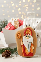 Photo of Composition with tasty gingerbread cookies on white wooden table against blurred lights. St. Nicholas Day celebration