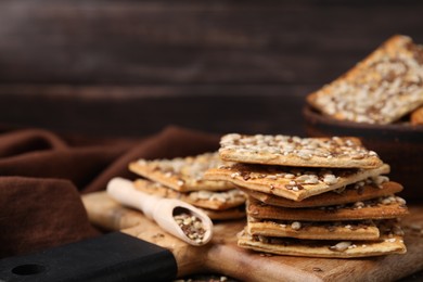 Photo of Cereal crackers with flax, sunflower and sesame seeds on wooden board, closeup. Space for text