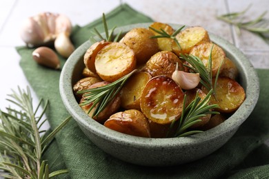 Tasty baked potato and aromatic rosemary in bowl on table, closeup