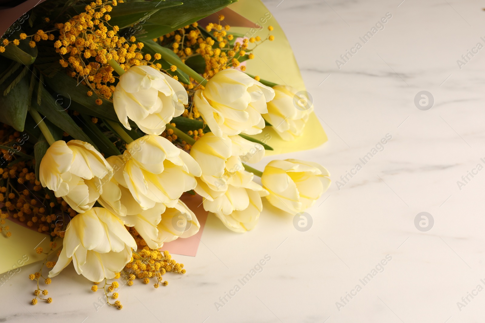 Photo of Bouquet with beautiful tulips and mimosa flowers on white marble table. Space for text