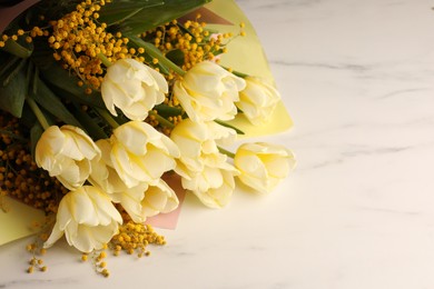 Bouquet with beautiful tulips and mimosa flowers on white marble table. Space for text