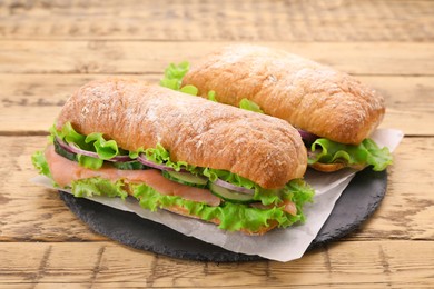 Photo of Delicious sandwiches with fresh vegetables and salmon on wooden table, closeup