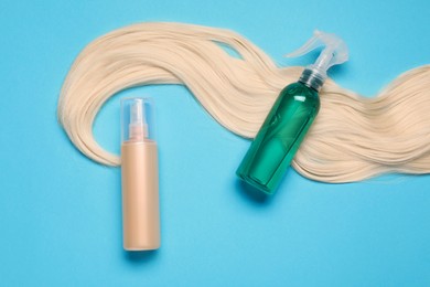 Photo of Spray bottles with thermal protection and lockblonde hair on light blue background, flat lay