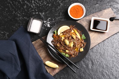 Photo of Stir-fry. Tasty noodles with vegetables and meat served on dark textured table, flat lay