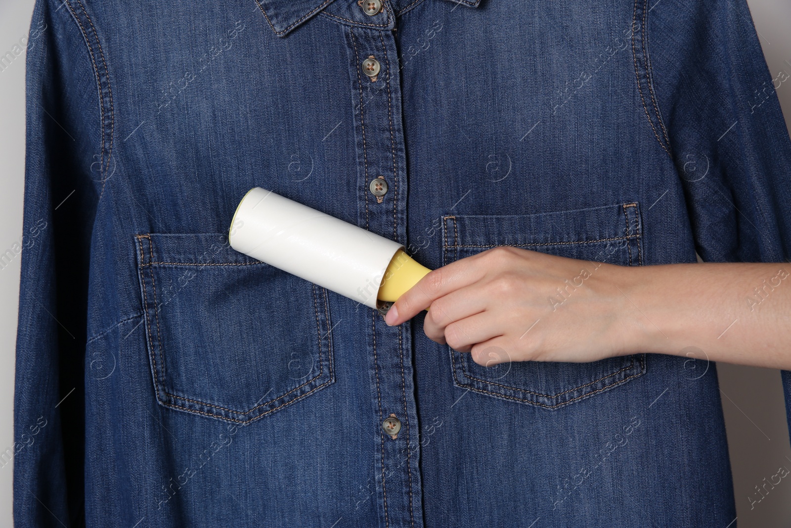 Photo of Woman cleaning denim shirt with lint roller, closeup