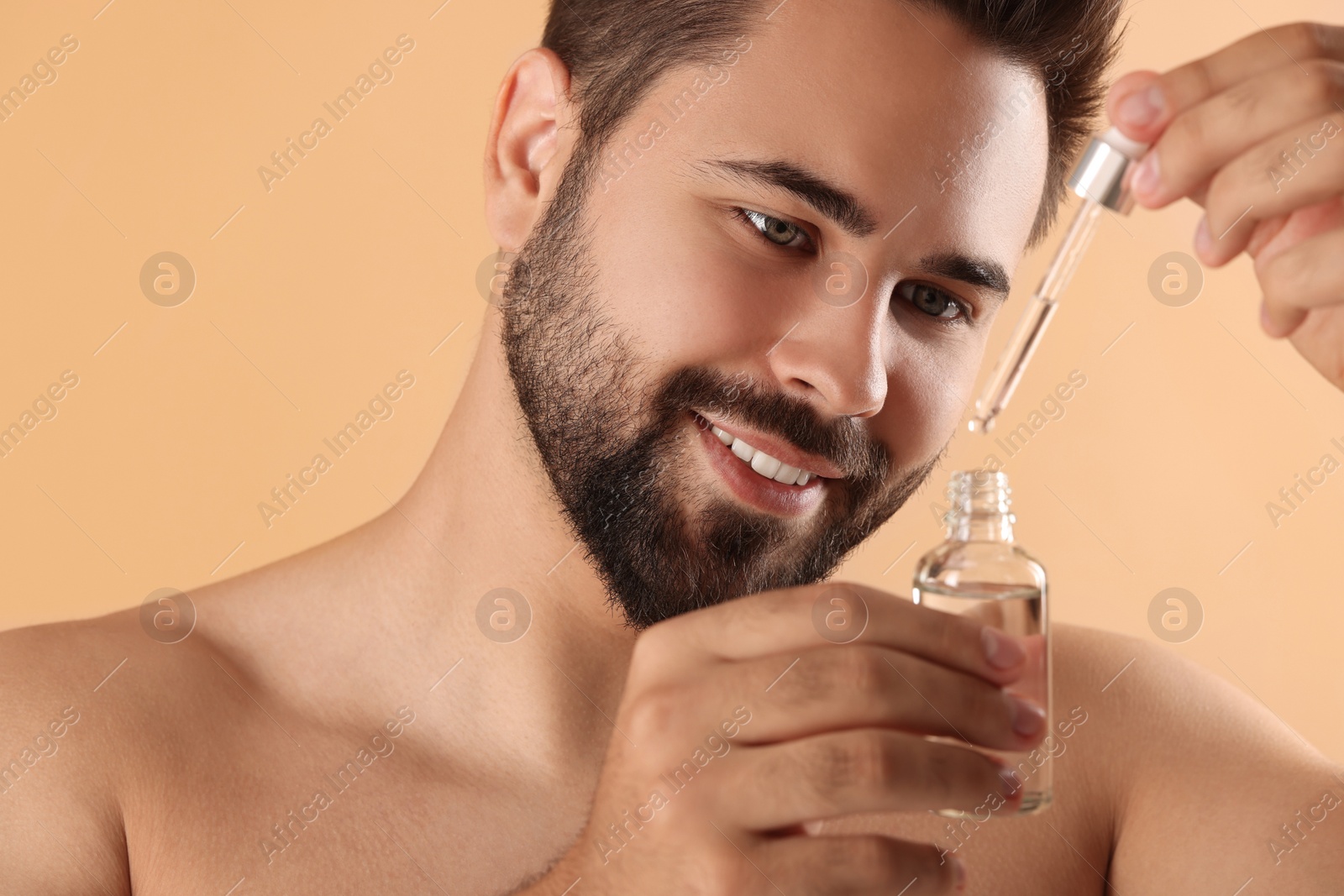 Photo of Handsome man with cosmetic serum in hands on beige background, closeup
