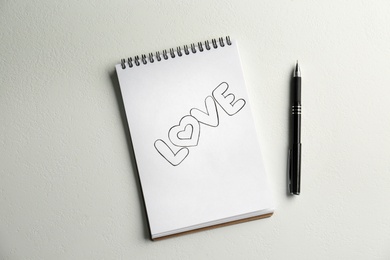 Photo of Notebook with handwritten word Love near pen on white background, flat lay