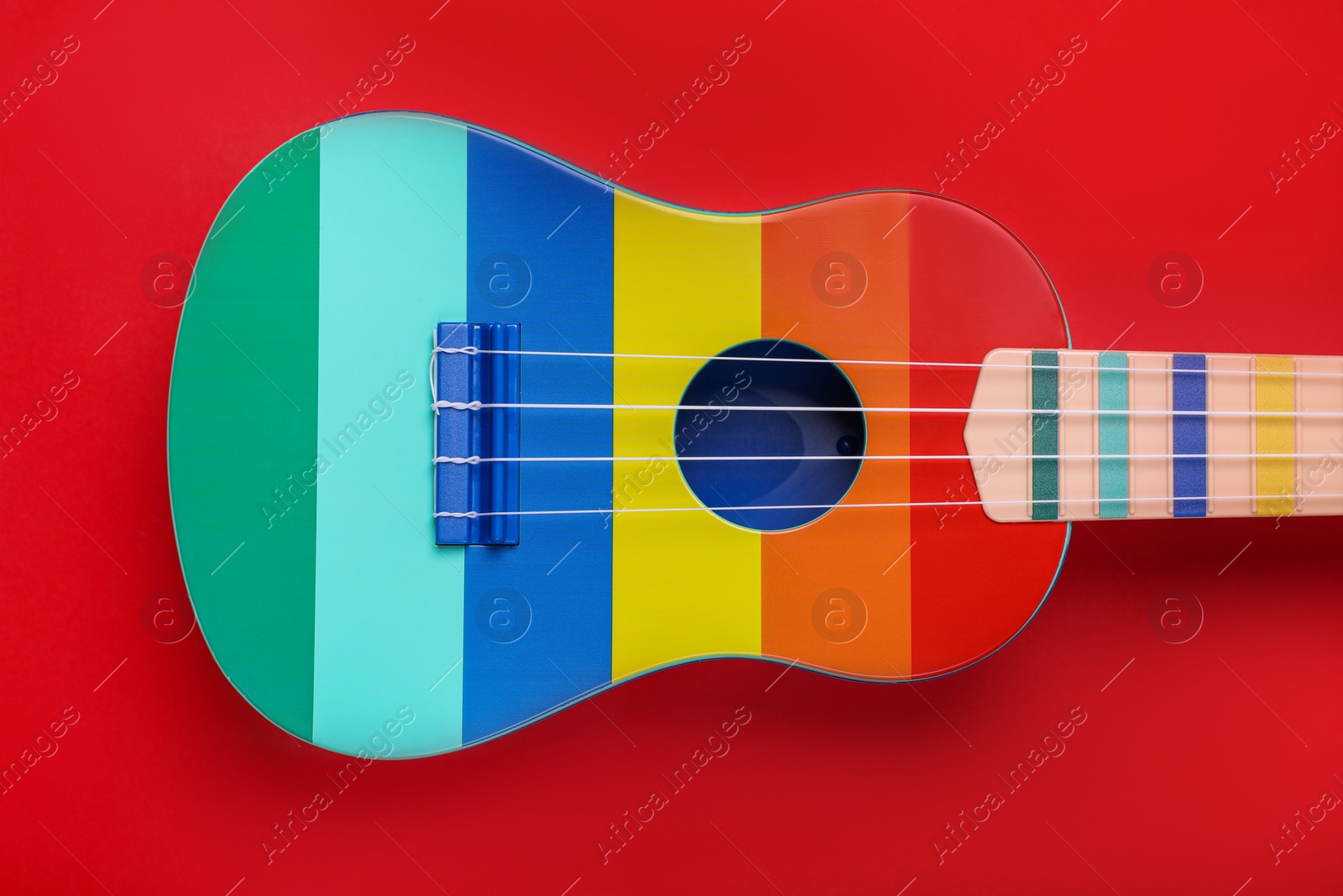 Photo of Colorful ukulele on red background, top view. String musical instrument