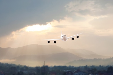 Image of Modern airplane flying in cloudy sky over hills