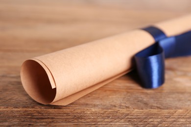 Photo of Rolled student's diploma with blue ribbon on wooden table, closeup