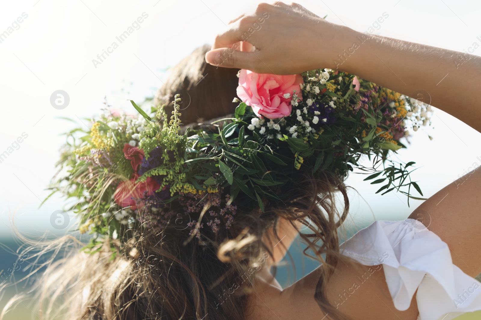 Photo of Young woman wearing wreath made of beautiful flowers outdoors on sunny day, closeup
