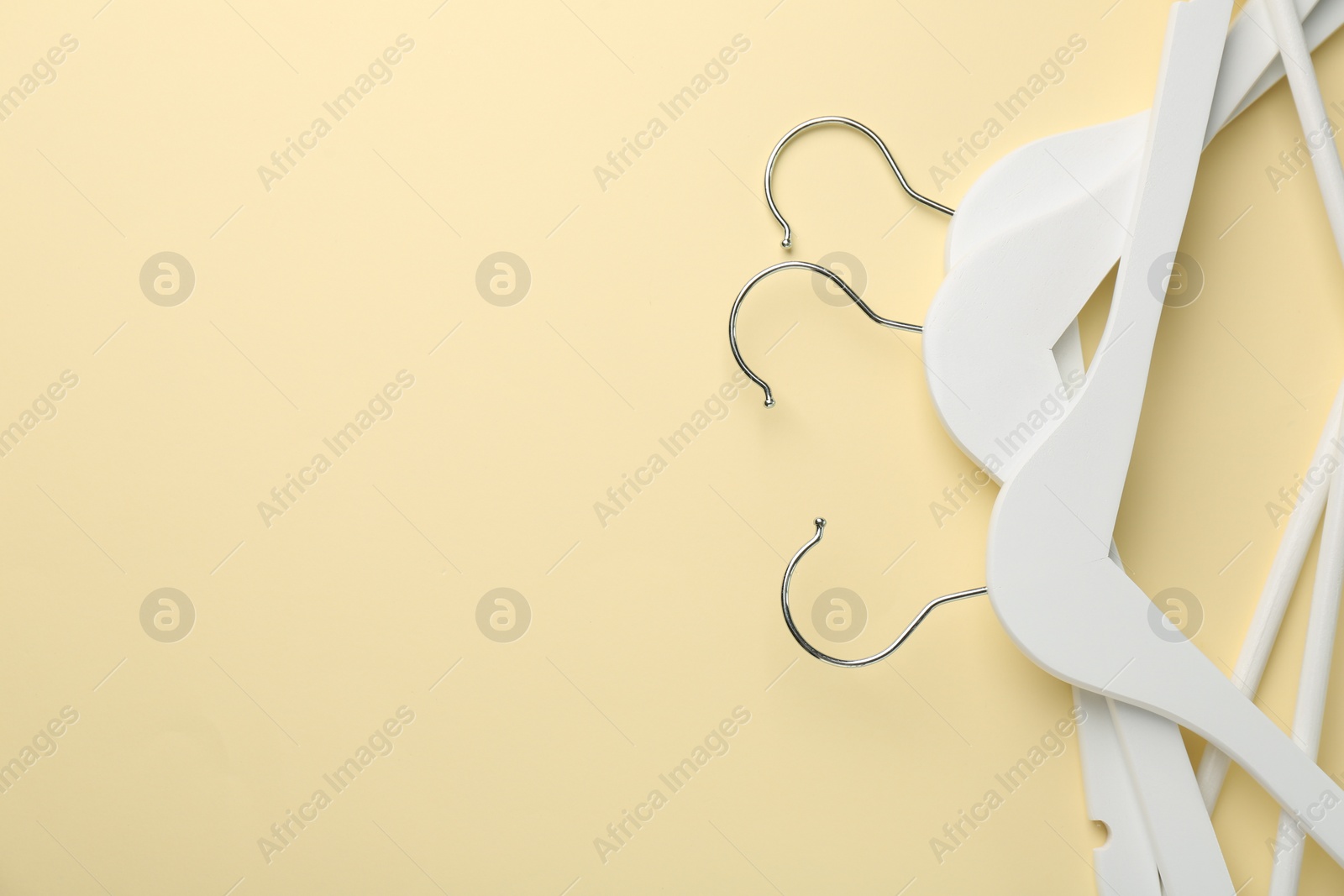 Photo of White hangers on pale yellow background, top view. Space for text