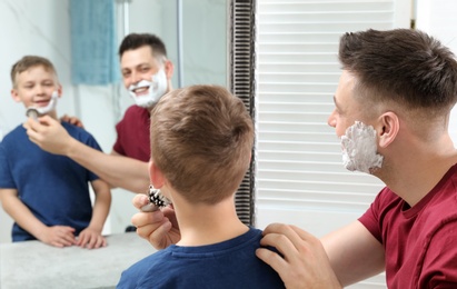 Photo of Dad applying shaving foam on son's face at mirror in bathroom