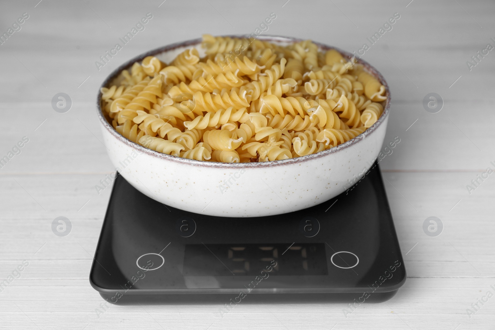 Photo of Electronic scales with uncooked pasta on white wooden table