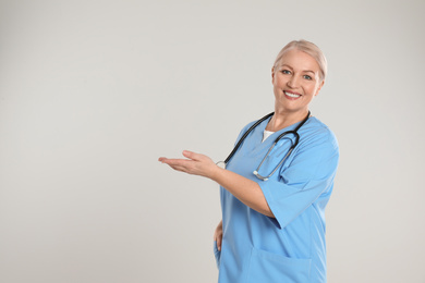 Portrait of mature doctor with stethoscope on light grey background. Space for text