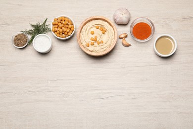 Bowl with delicious hummus and different ingredients on white wooden table, flat lay. Space for text