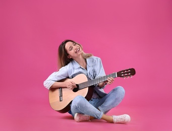 Young woman playing acoustic guitar on color background