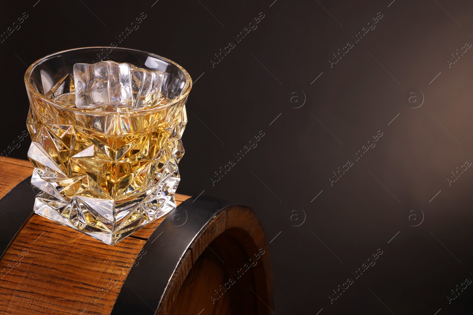 Photo of Whiskey in glass on wooden barrel against dark background, space for text