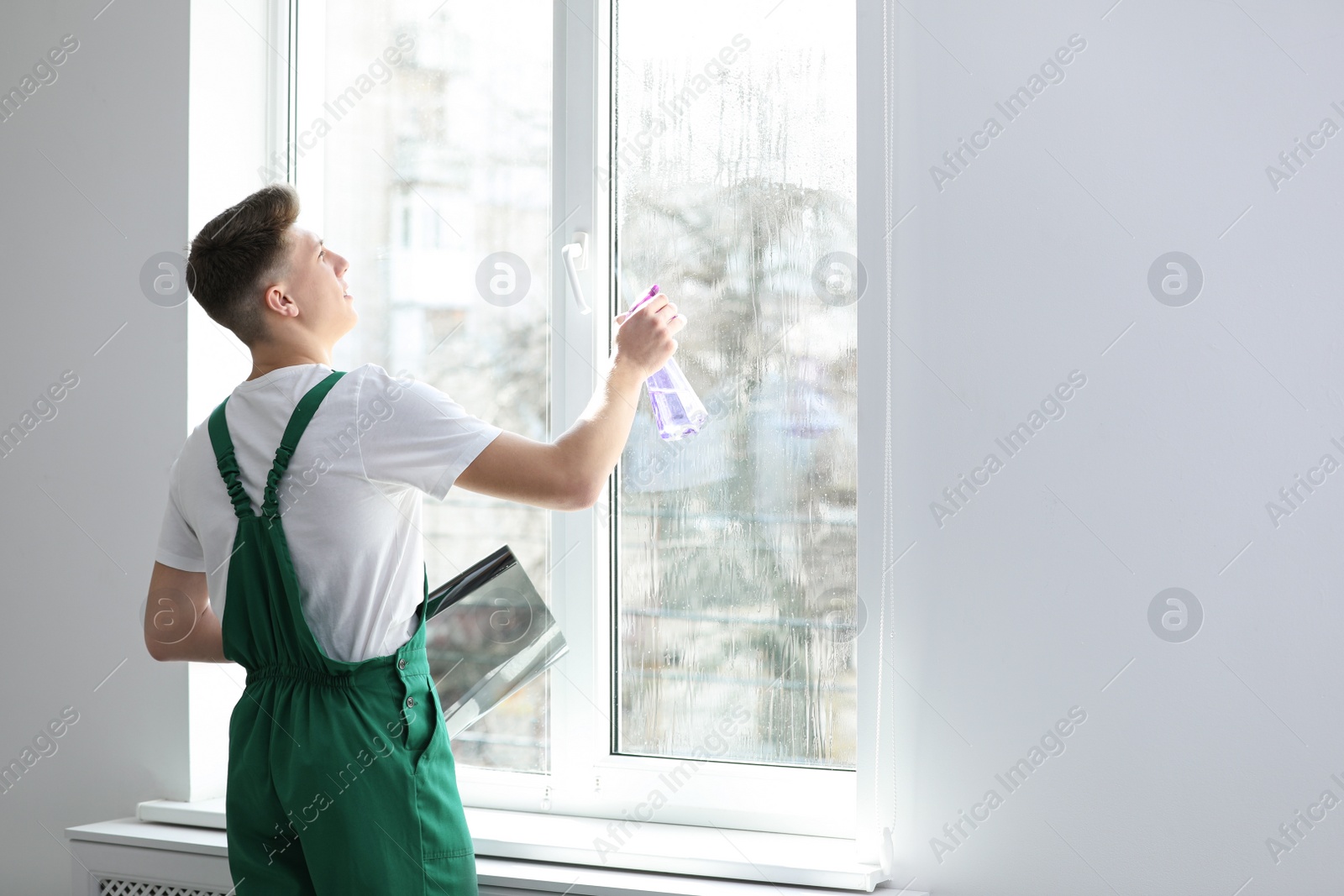 Photo of Young worker tinting window with foil indoors. Space for text