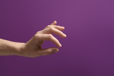 Woman holding something in hand on purple background, closeup. Space for text