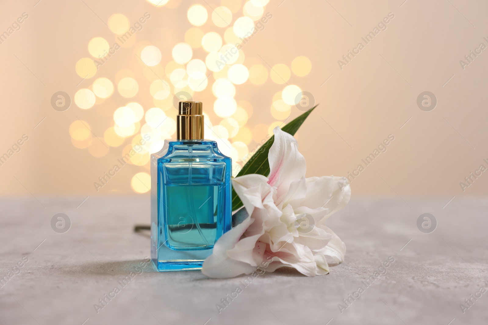 Photo of Bottle of perfume and beautiful lily flower on table against beige background with blurred lights