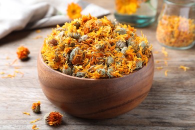 Bowl of dry calendula flowers on wooden table, closeup