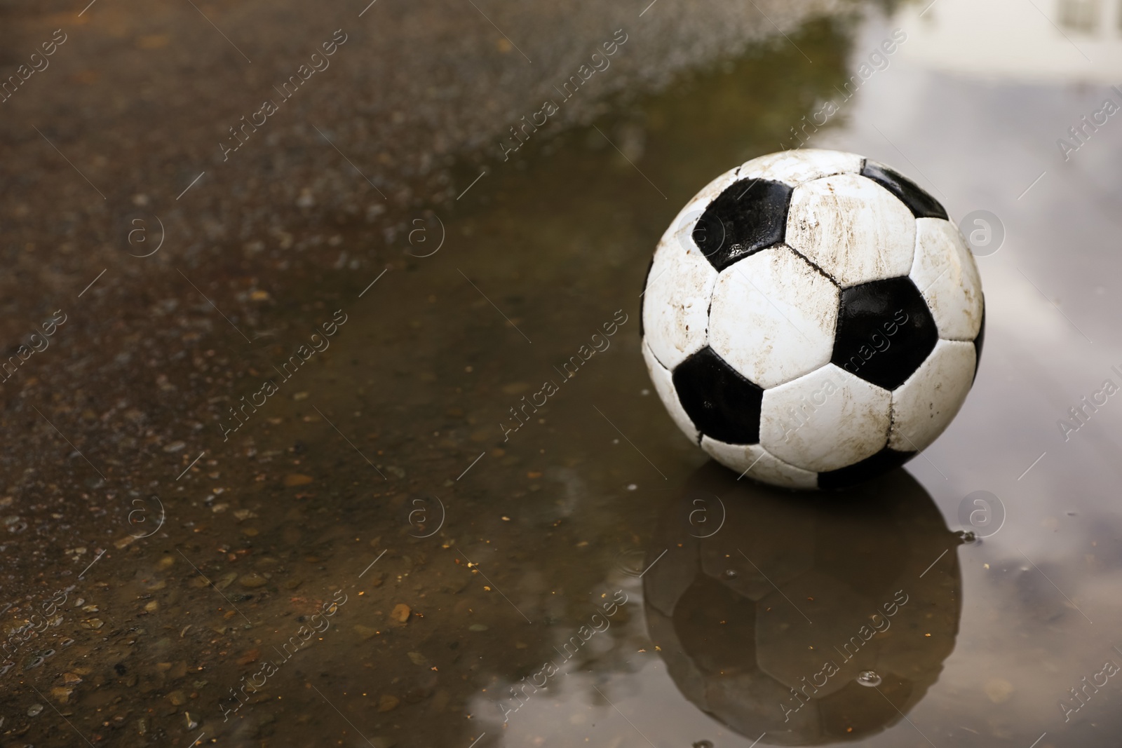 Photo of Dirty soccer ball near puddle outdoors, space for text