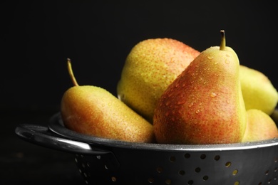 Photo of Colander with pears against black background, closeup