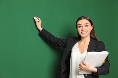Photo of Portrait of young teacher with notebook and chalk on green background. Space for text