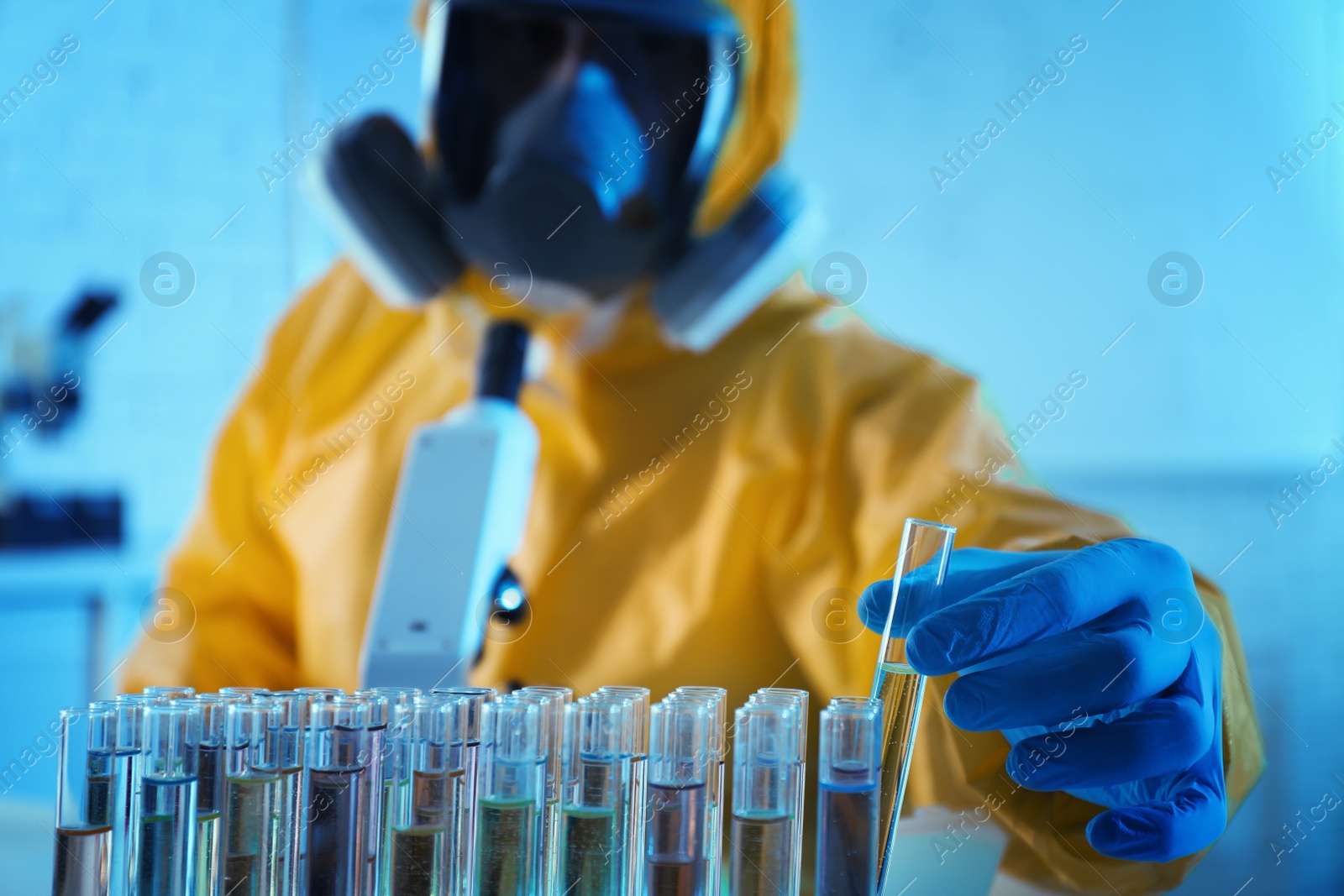 Photo of Scientist in chemical protective suit taking test tube out of rack at laboratory, focus on hand. Virus research