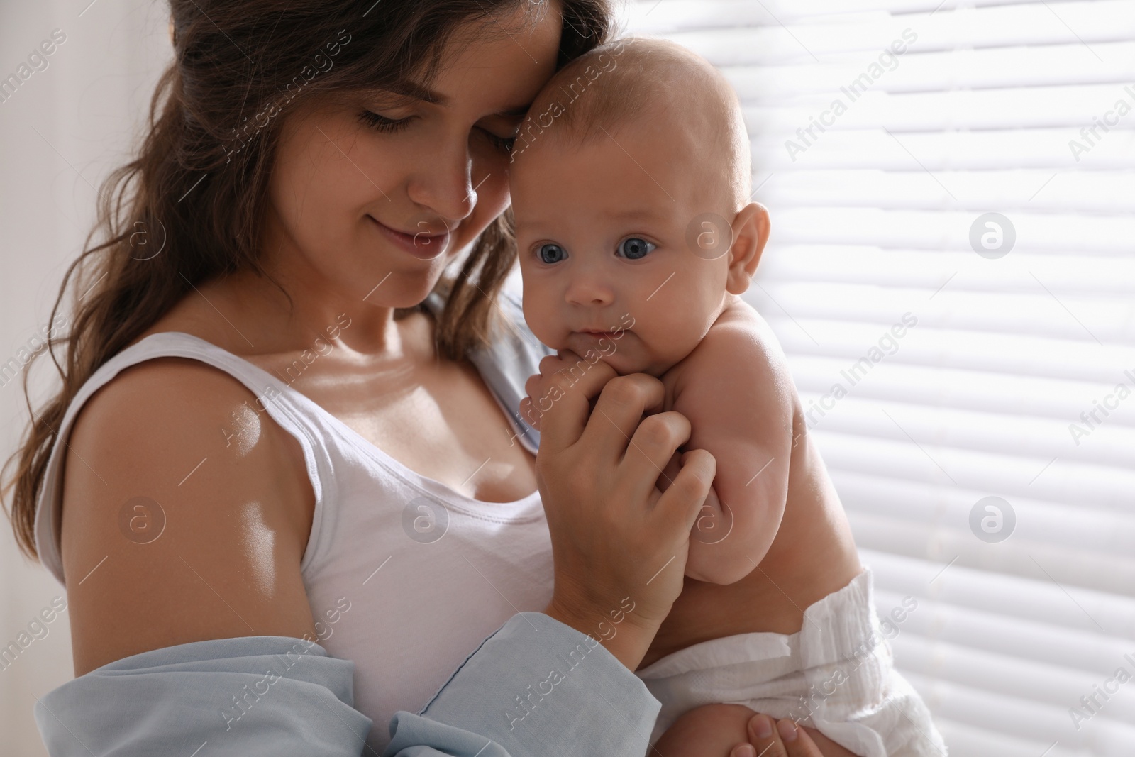 Photo of Happy young mother with her cute baby near window at home