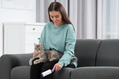 Photo of Pet shedding. Woman with lint roller removing cat`s hair from trousers on sofa at home