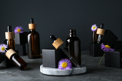 Photo of Bottles of essential oil and beautiful flowers on dark gray stone table
