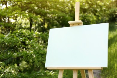 Photo of Wooden easel with blank canvas in picturesque countryside
