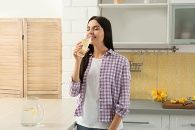 Photo of Beautiful young woman drinking lemon water in kitchen