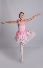 Photo of Beautifully dressed little ballerina dancing on grey background