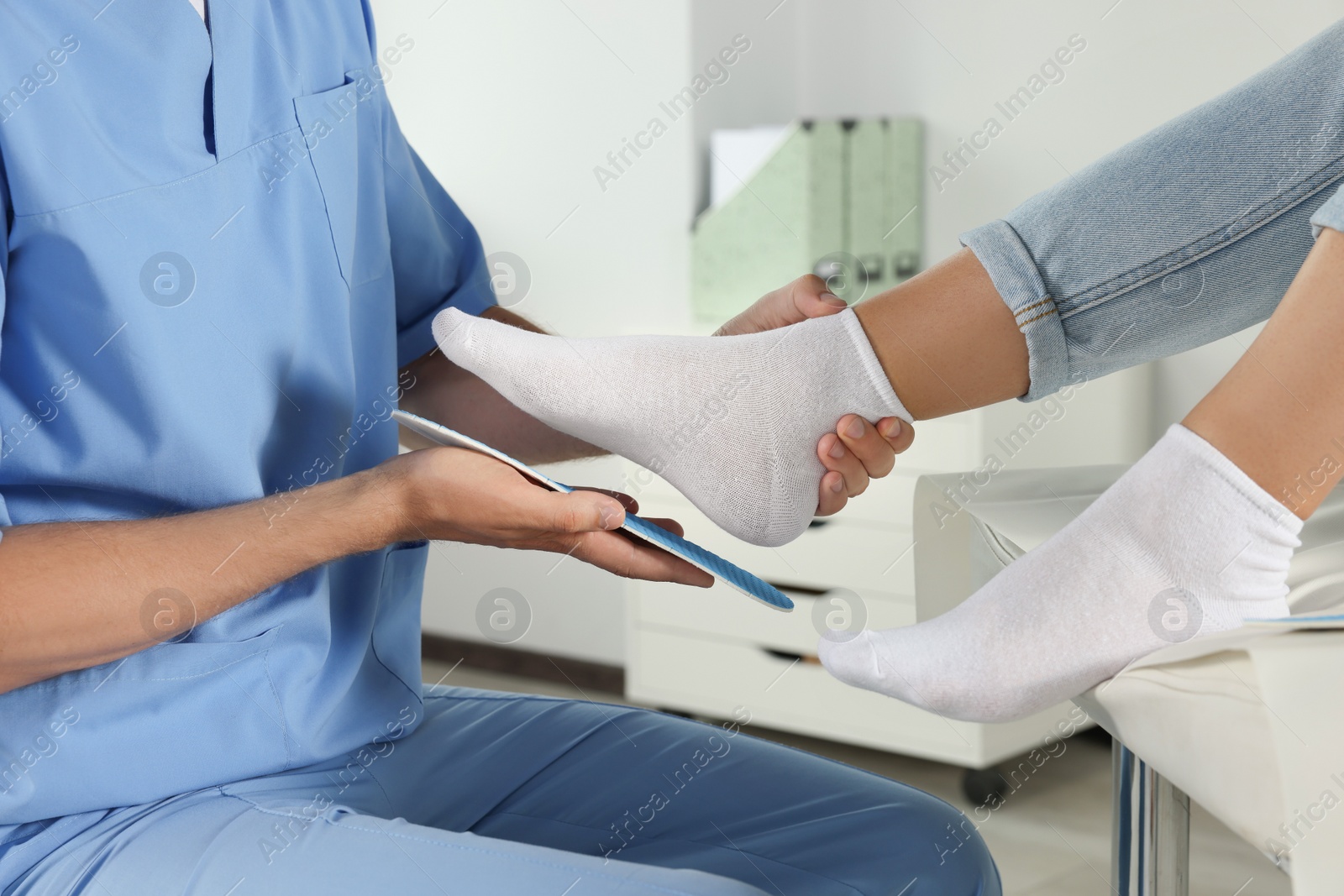 Photo of Male orthopedist fitting insole to patient's foot in hospital, closeup