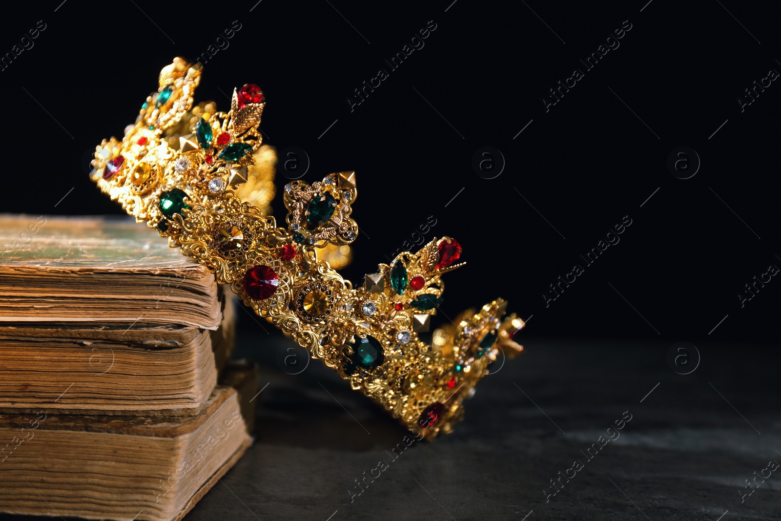 Photo of Beautiful golden crown and old books on black table, space for text. Fantasy item